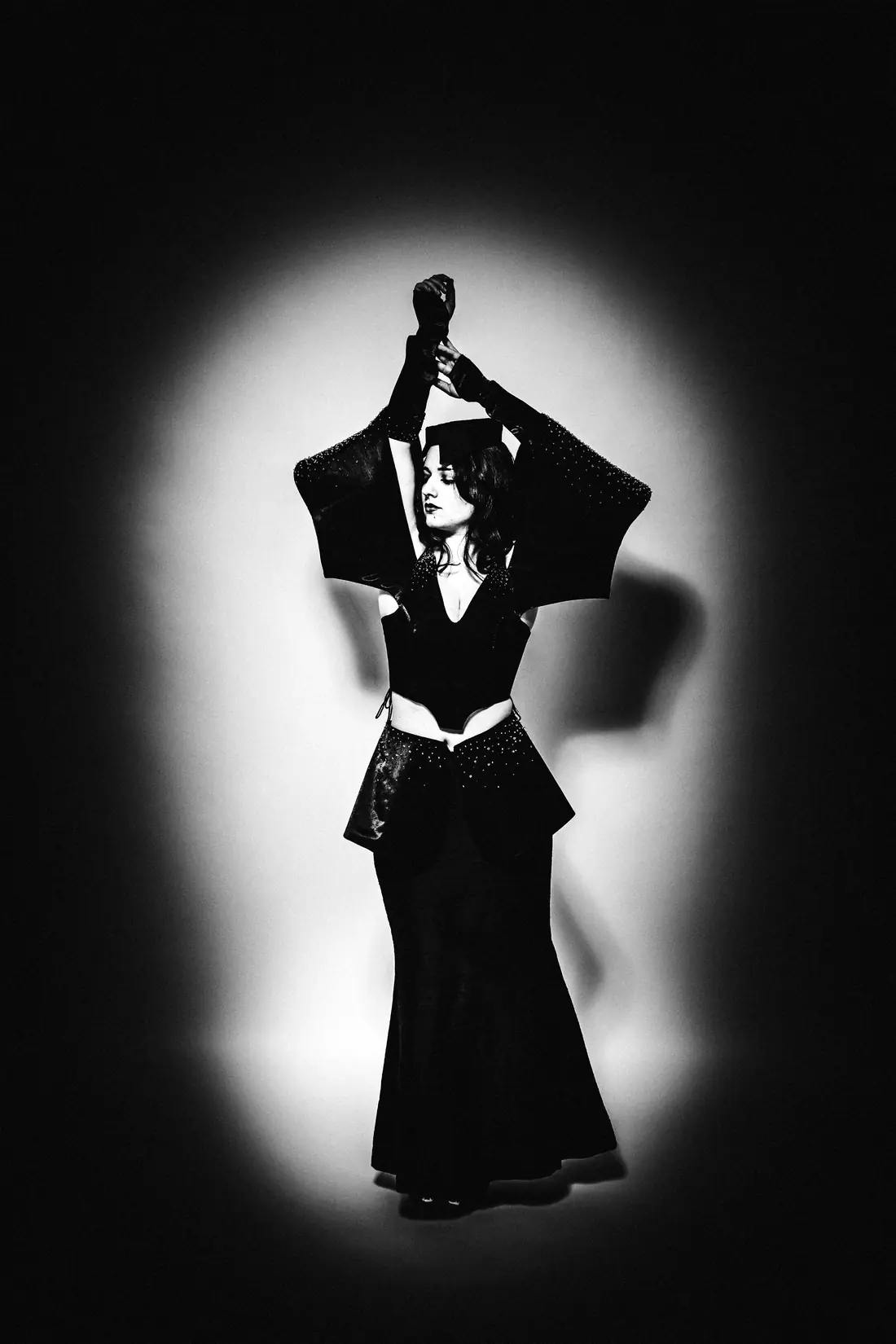 The collar dress: arms raised beneath the sculpted headpiece, lit by a single spotlight.